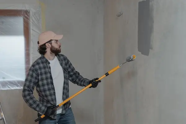 Painter rolling grey paint onto an interior wall in Spokane